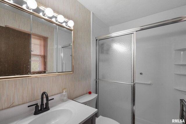 full bathroom with toilet, wallpapered walls, a shower with shower door, and vanity
