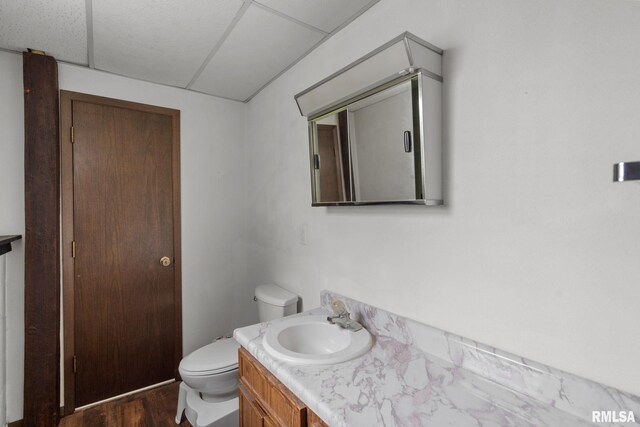 half bathroom featuring vanity, a drop ceiling, toilet, and wood finished floors