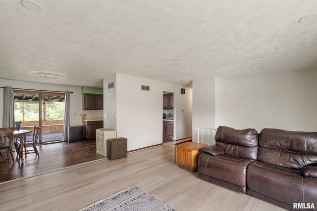living room with a textured ceiling, visible vents, and light wood finished floors
