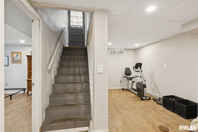 staircase featuring a paneled ceiling, recessed lighting, and wood finished floors