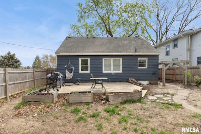 rear view of house with a fenced backyard, a wooden deck, a garden, and roof with shingles