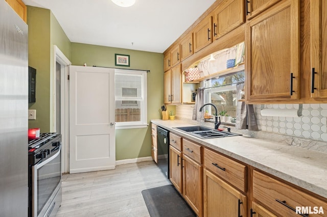 kitchen with backsplash, a sink, baseboards, black appliances, and light wood-style floors