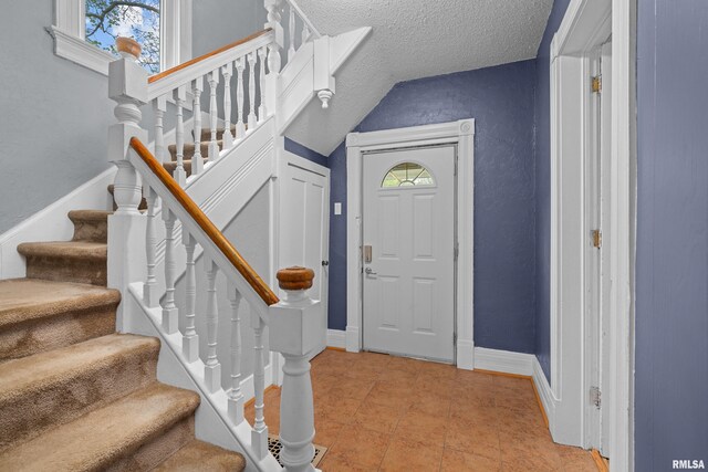 entrance foyer featuring a textured ceiling, vaulted ceiling, light tile patterned floors, baseboards, and stairs