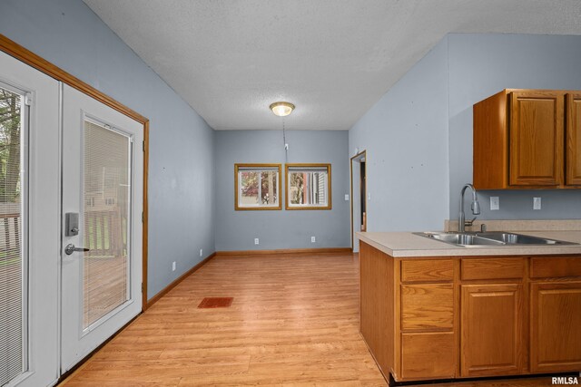 kitchen featuring a textured ceiling, brown cabinets, a sink, light countertops, and light wood-style floors