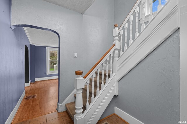 staircase featuring arched walkways, a textured ceiling, visible vents, and baseboards