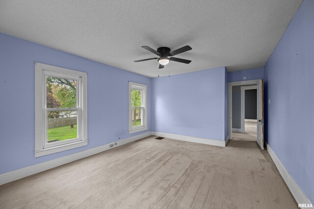 carpeted spare room featuring a ceiling fan, a textured ceiling, visible vents, and plenty of natural light