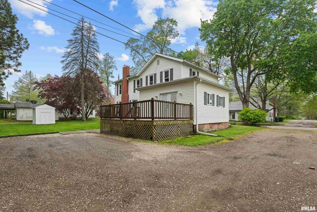 back of property with an outdoor structure, a wooden deck, a chimney, a lawn, and a storage shed
