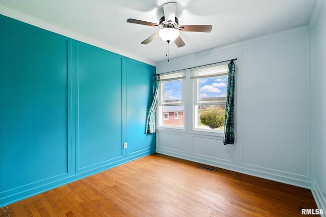 empty room with ceiling fan, visible vents, crown molding, light wood finished floors, and a decorative wall