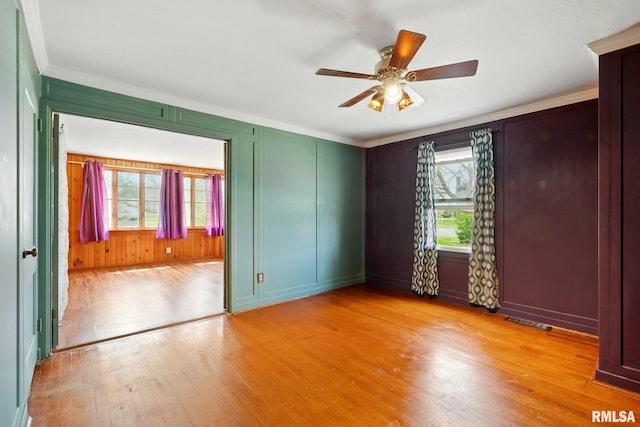unfurnished room with crown molding, light wood finished floors, a decorative wall, a ceiling fan, and visible vents