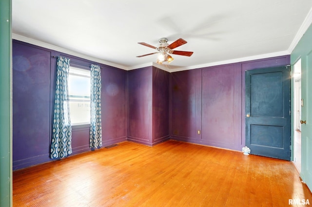 empty room featuring light wood-type flooring, crown molding, ceiling fan, and a decorative wall
