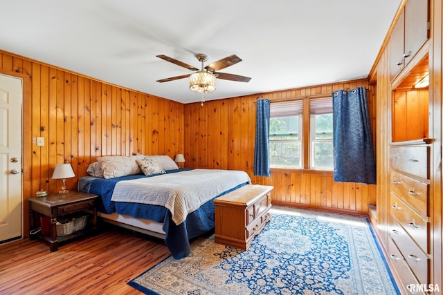 bedroom with wooden walls, a ceiling fan, and light wood-style flooring