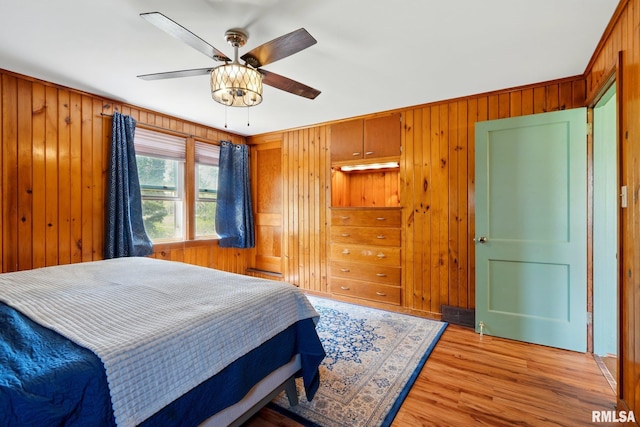 bedroom featuring wooden walls, a ceiling fan, and light wood-type flooring