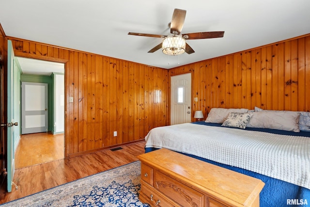 bedroom with light wood-style floors, wood walls, ceiling fan, and visible vents