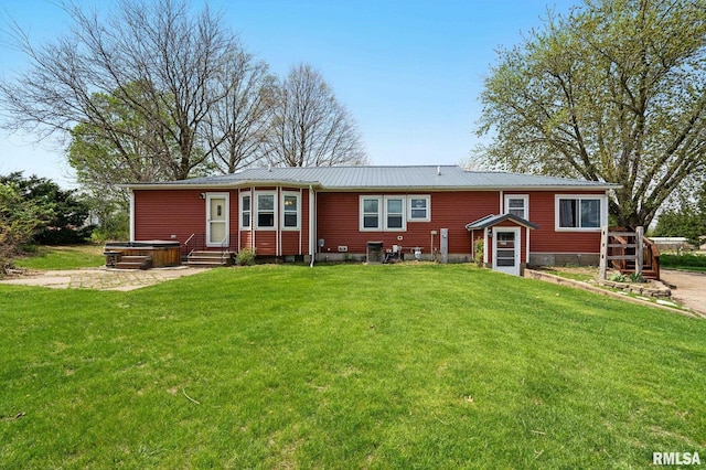 back of property with a lawn, a hot tub, entry steps, and metal roof