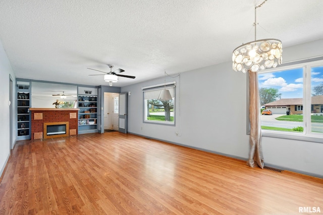 unfurnished living room with light wood-style flooring, a textured ceiling, ceiling fan with notable chandelier, and a fireplace