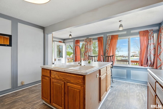 kitchen with light countertops, brown cabinetry, a sink, and an island with sink