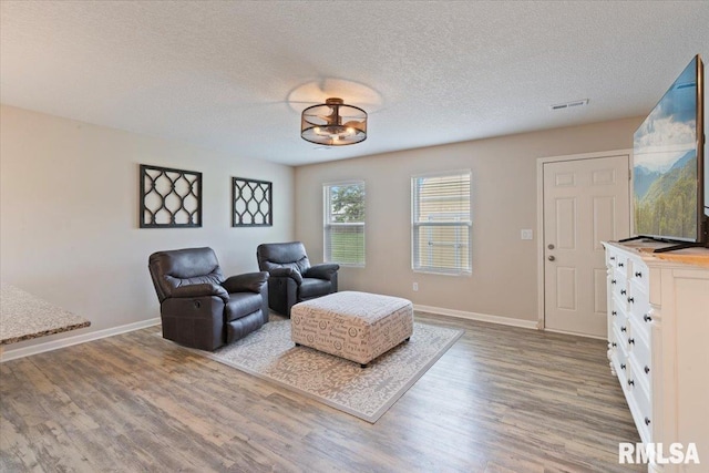 living area featuring visible vents, a textured ceiling, baseboards, and wood finished floors