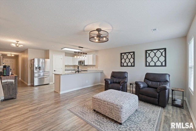 living area with baseboards, a textured ceiling, light wood finished floors, and a notable chandelier