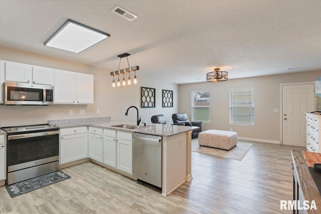 kitchen featuring visible vents, appliances with stainless steel finishes, a sink, light wood finished floors, and open floor plan