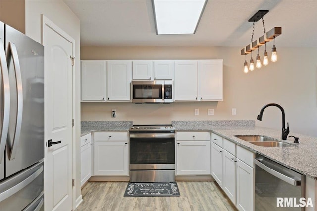kitchen with white cabinets, appliances with stainless steel finishes, a sink, and light wood-type flooring