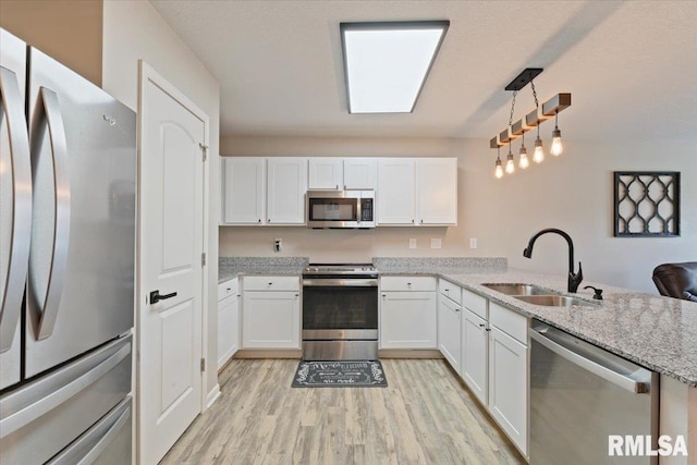 kitchen with appliances with stainless steel finishes, a sink, light stone counters, white cabinets, and light wood-style flooring