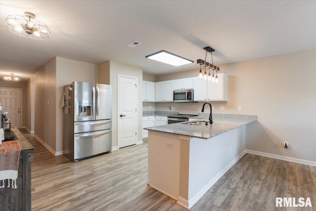 kitchen featuring light stone counters, a sink, light wood finished floors, stainless steel appliances, and a peninsula