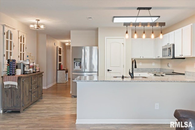 kitchen with appliances with stainless steel finishes, light wood-style flooring, a peninsula, and light stone counters