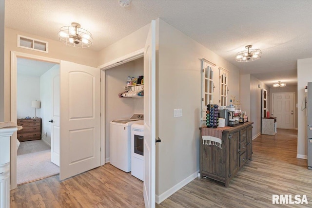 hallway with light wood-style floors, visible vents, washer and clothes dryer, and a chandelier