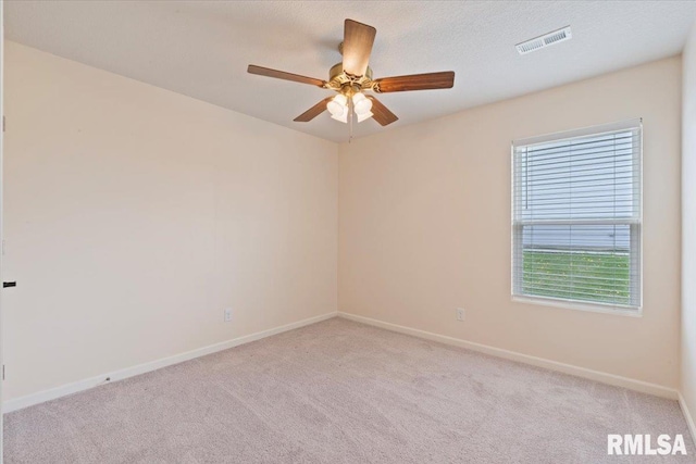 spare room with light colored carpet, a ceiling fan, visible vents, and baseboards