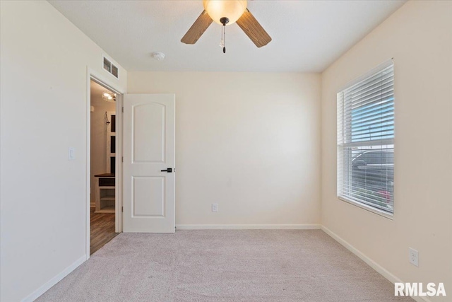 carpeted spare room featuring baseboards, a ceiling fan, and visible vents