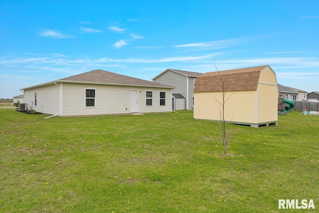 back of property featuring a lawn, a shingled roof, an outdoor structure, and a storage unit