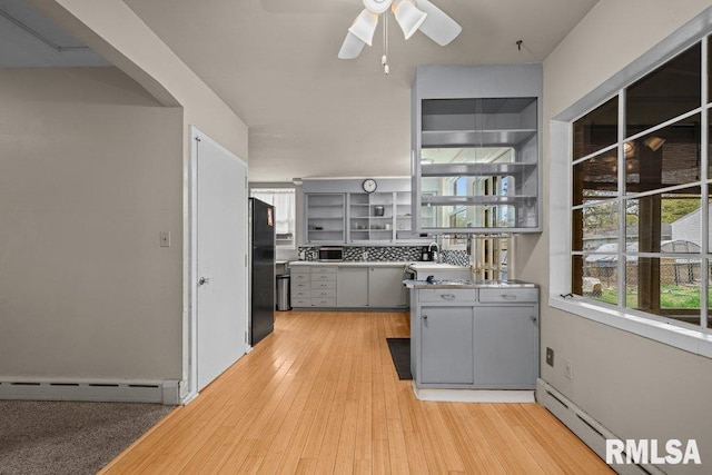 kitchen featuring a ceiling fan, baseboard heating, gray cabinetry, freestanding refrigerator, and a wealth of natural light