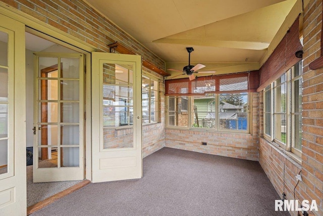 unfurnished sunroom featuring carpet, ceiling fan, brick wall, and a healthy amount of sunlight