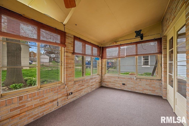 unfurnished sunroom with vaulted ceiling, a ceiling fan, carpet flooring, and brick wall