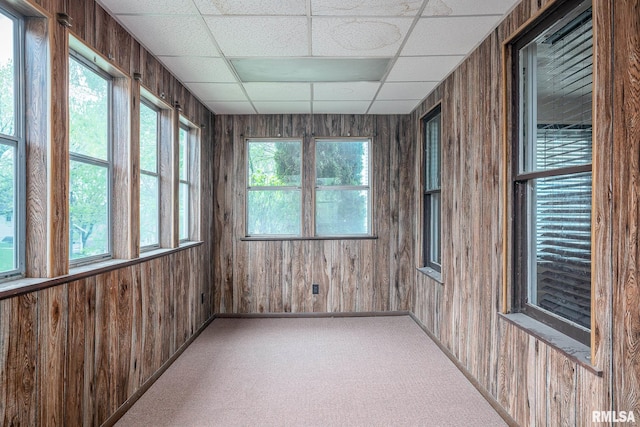 unfurnished sunroom featuring baseboards, carpet, wood walls, and a paneled ceiling