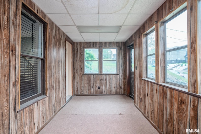 empty room with wooden walls, baseboards, light colored carpet, and a paneled ceiling