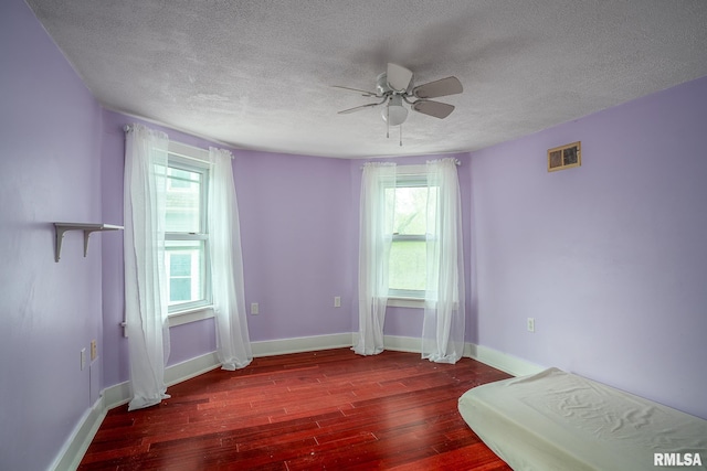 unfurnished bedroom with visible vents, a textured ceiling, wood finished floors, and multiple windows