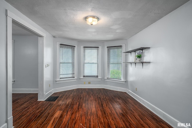 empty room with a textured ceiling, baseboards, and wood finished floors
