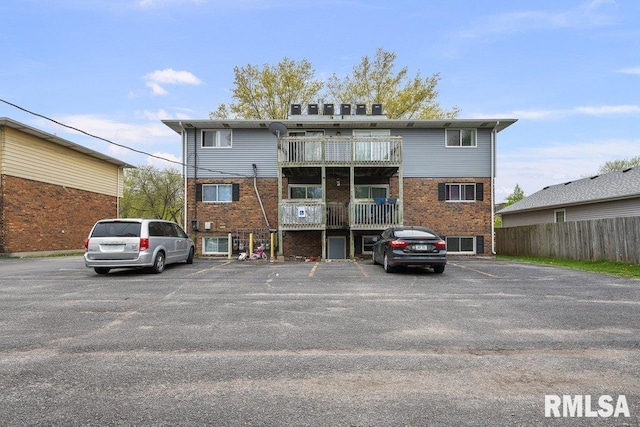 back of property featuring brick siding, uncovered parking, and fence