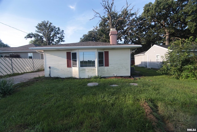 rear view of house featuring fence, a chimney, and a lawn