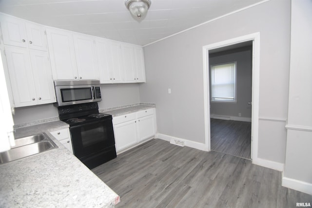 kitchen featuring black electric range oven, a sink, light countertops, stainless steel microwave, and white cabinetry