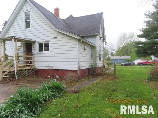 view of side of home with roof with shingles, a chimney, and a yard