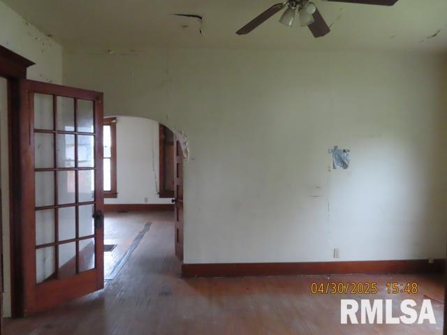 unfurnished room featuring baseboards, arched walkways, a ceiling fan, and wood finished floors