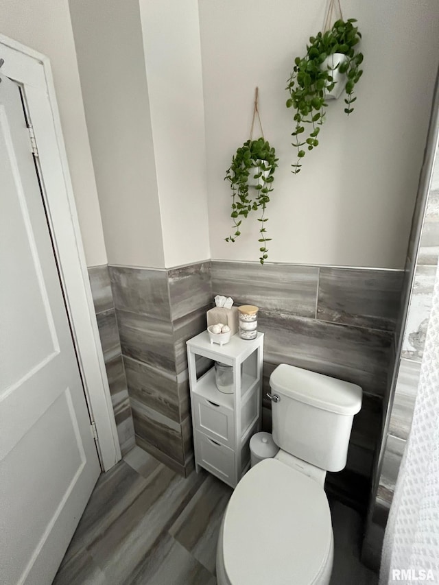 bathroom with wood finished floors, a wainscoted wall, toilet, and tile walls