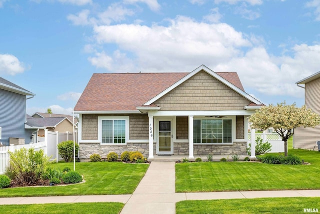 craftsman house featuring fence, a front lawn, and stone siding