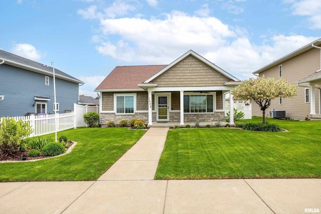 craftsman-style home featuring covered porch, fence, cooling unit, a front lawn, and stone siding