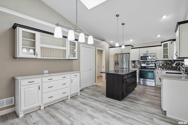 kitchen with appliances with stainless steel finishes, a sink, vaulted ceiling with skylight, a center island, and visible vents