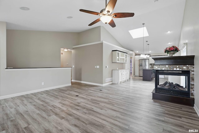 living room with visible vents, baseboards, light wood-type flooring, a ceiling fan, and a skylight