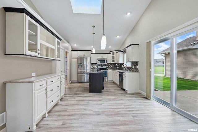 kitchen with lofted ceiling with skylight, a center island, tasteful backsplash, a sink, and appliances with stainless steel finishes