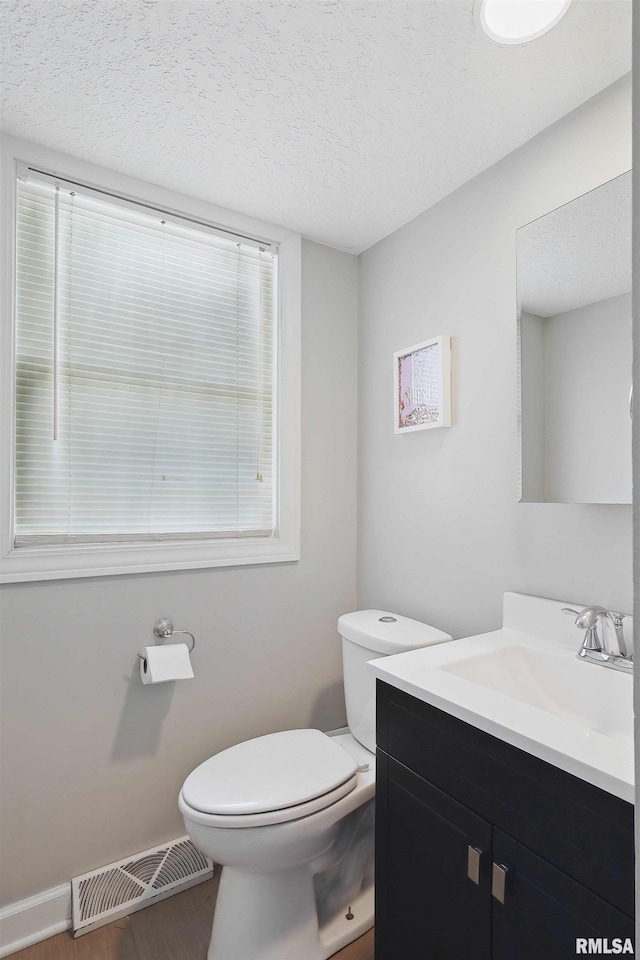 half bathroom featuring vanity, toilet, a textured ceiling, wood finished floors, and visible vents
